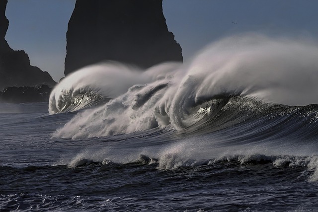 Vega options greek: a large ocean wave breaking in strong wind beside dark sea stacks