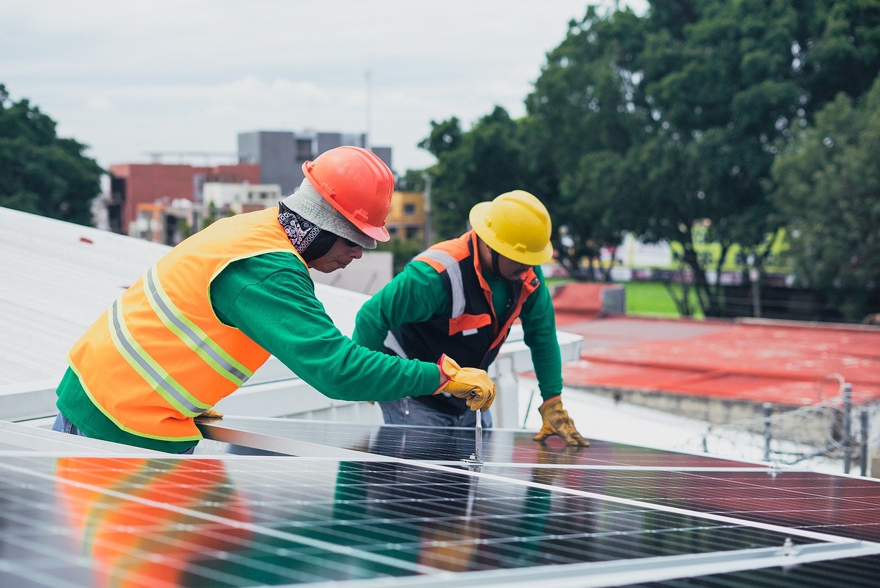 Waaree Renewable Q2 results: two workers in hard hats and safety vests installing solar panels on a rooftop